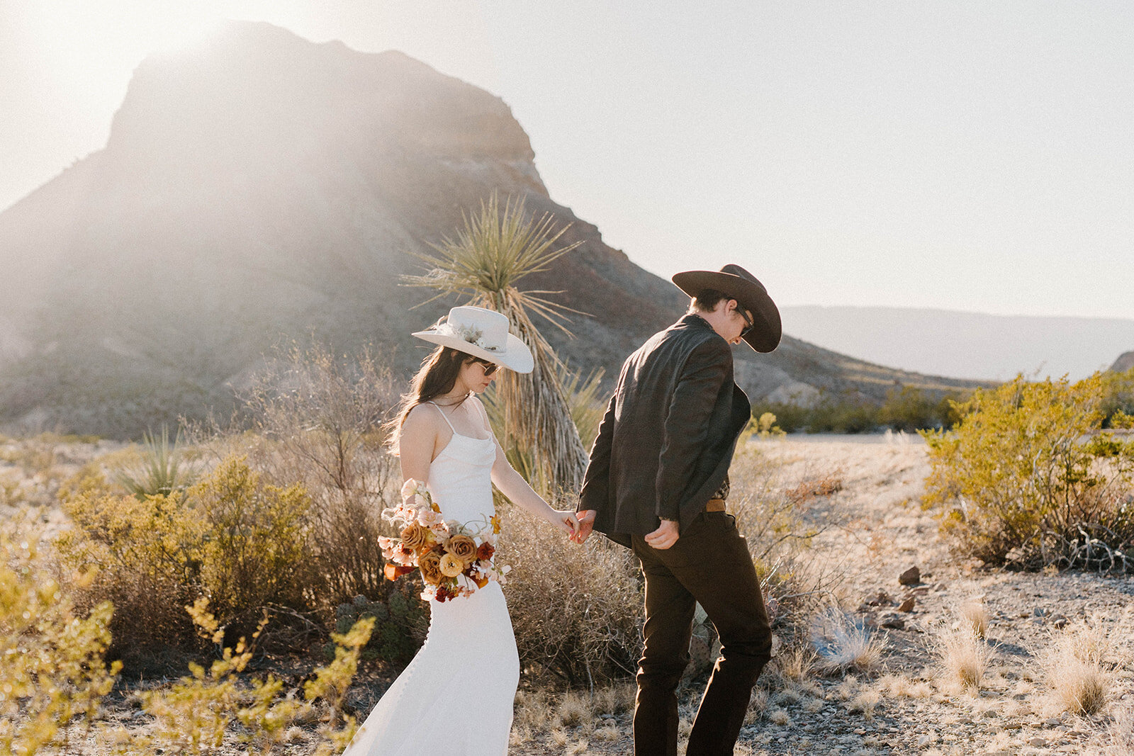 A couple walking through the desert in West Texas, eloping and holding a bouquet of flowers.