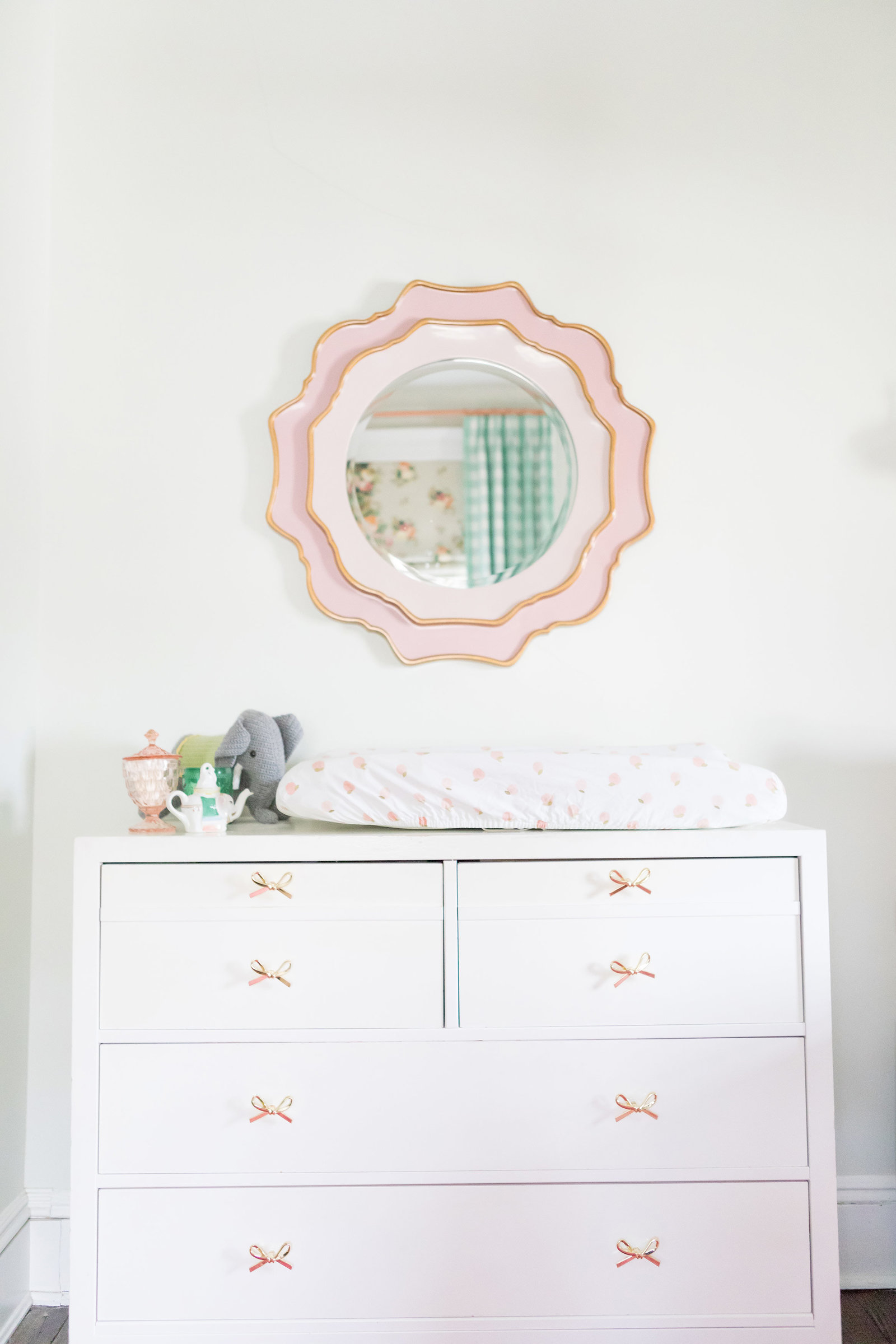 A white dresser with bow pulls and a round mirror.