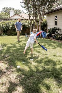 A father and son play baseball in the backyard