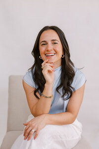 Woman sitting on a chair and smiling with her hand on her chin, while posing for her bay area branding photography photoshoot