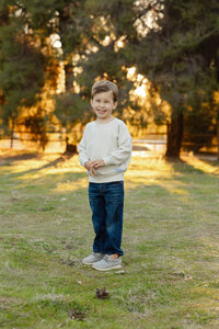 Young boy standing alone in a grassy field with warm sunset light behind him, natural child portrait captured by Kaitlyn Dawn Photography, Yucaipa family photographer.