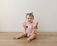 Pink romper, sweet smile, and a heart full of birthday joy. Captured by Yucaipa cake smash photographer Kaitlyn Dawn Photography.