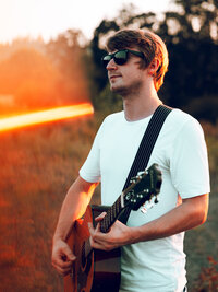 Independent music artist photographed outdoors with a guitar in warm golden light.