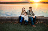 Three siblings sitting together by the waterfront during a New Bern family photography session