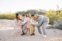 The Collins family sharing a playful candid moment in the Las Vegas desert, with parents laughing and interacting with their three young children during a fun, natural golden hour family photo session.