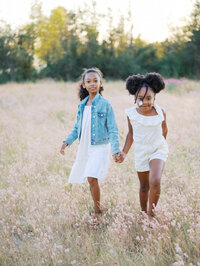 Sisters holding hands and walking in a grassy field