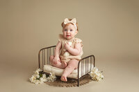 One year old girl sitting on a bed during her One Year Milestone session at Jennifer Brandes Photography studio near Mankato, Minnesota.