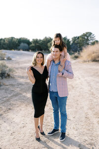 The Parker family posing together in the Las Vegas desert, with father holding their young daughter on his shoulders and mother standing beside them, captured in a warm, natural light family portrait session.