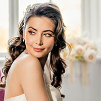 A bride in an off-shoulder gown standing near sheer curtains, softly lit by window light, captured in a calm and reflective moment by a UK wedding photographer.