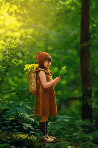 A young girl stands in a magical forest setting carrying a backpack of daffodils while being photographed by Kara Reese of Waukesha, WI.