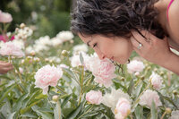 woman leans down to smell light pink peony at gardens in nichols arboretum in ann arbor michigan