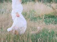 Action view of a pregnant woman walking in a grassy field