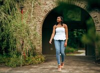 Senior portrait at Bella Sera Gardens in Loxley, Alabama — holding her necklace with one hand,
the other hand above her head, archway behind her.
