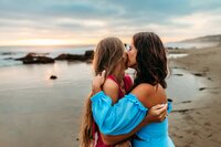 mom kissing daughter's cheek at the beach