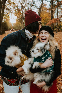 man and woman holding dogs while laughing and standing outside