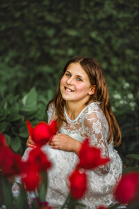 Young girl smiling in a garden with vibrant red flowers in the foreground
