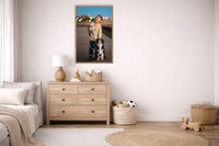 Vertical framed portrait of young boy holding leash beside dog at blue hour in downtown New Bern displayed above dresser in bright child’s bedroom