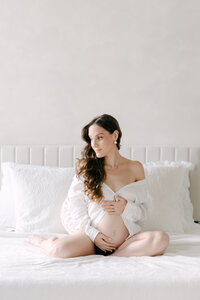 Pregnant mom in white shirt on a bed in white Miami studio
