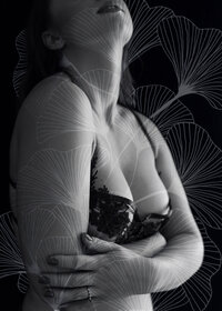 A black and white boudoirimage overlaid with a ginkgo leaf illustration of a woman wearing a black lace bra who appears to be hugging herself.