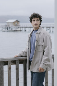Model in an oatmeal fleece overshirt over a blue tee with straight denim, at the dock railing
