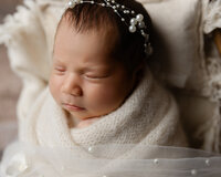 Close-up portrait of a sleeping newborn baby girl wearing a delicate pearl headband and wrapped in a soft white blanket during an elegant newborn photography session photographed by Kaitlyn Dawn Photography.