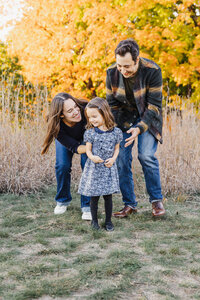 mom and dad bending down to tickle their young daughter during photo session in High Park