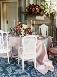 long wedding table with white chairs, blush linen, floral arrangements, candles, and fireplace backdrop in a romantic French style