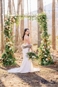 Bride with winter bouquet beside foraged greenery arbor by Flowergirl Cville at woodland styled shoot near Charlottesville | Photo by Xiaoqi Li Photography