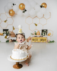 Adorable little one tasting every bit of her bee-themed birthday cake, surrounded by sweet honey details and golden giggles. Captured by Yucaipa cake smash photographer Kaitlyn Dawn Photography.