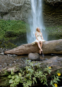 Oregon City high school senior sitting on the log in front of latourell falls for her senior portraits.
