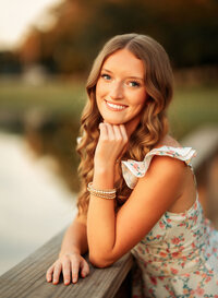 Senior portrait in downtown Magnolia Springs, Alabama — leaning on a railing with the pond reflecting behind her.