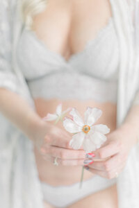 Close up in studio boudoir detail shot of a woman wearing light grey lingerie as she holds fresh flowers in front of her.