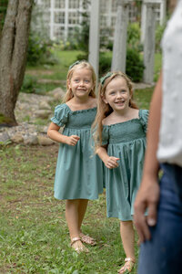 young sisters look mischeviously at parents at rustic wild arrow in summer