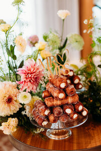 Mr and Mrs cake topper placed in a tower of Italian cannoli with flower arrangements in the background