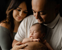 Parents gently holding their sleeping newborn baby during an intimate studio newborn photography session with newborn photographer Kaitlyn Dawn Photography.