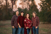 Family of four standing together in wooded setting during outdoor portrait session in North Carolina