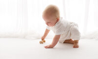 Baby plays with a wooden toy during Baby Milestone Portrait Session at Holy City Babies Portrait Studio in Charleston, SC.
