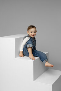 Young girl sitting barefoot on white studio blocks with a soft gray background, natural light studio child portrait photographed by Kaitlyn Dawn Photography.