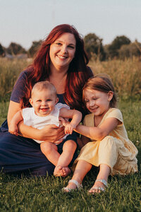Mother sitting with her baby and daughter in a grassy field during a Cleveland family photography session