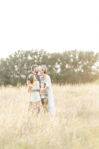 Family of 4 photo of them all standing together in an open grassy park in Dallas as they cold each other and pose for their photographer.