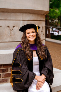 Law school grad wearing Vanderbilt Master's robes sitting on bench outside building