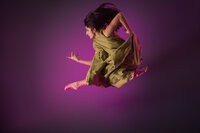A woman in a green dress leaps gracefully in midair against a purple background, her hair and dress flowing in motion—a stunning image captured by a creative portrait studio Washington DC known for dynamic dance photography.