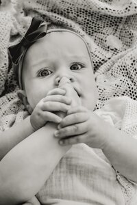 A six month old baby chews on her foot while laying on a blanket in a park in Plano Texas