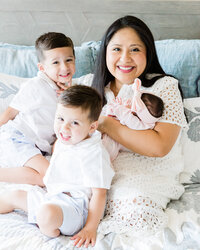 Mother smiling with her two young sons while holding their newborn baby during an in-home lifestyle newborn session.