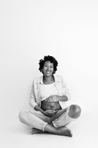 expecting mother holding baby bump seated during soft-lit maternity photography session in North Hollywood studio