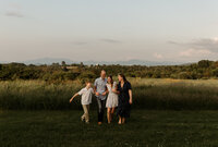 A family of four runs and plays together at sunset in Maine, full of laughter and energy. Fine art lifestyle family photography by Damini Photography capturing joyful, candid, and warm moments