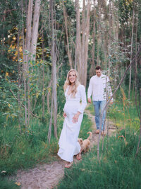 Pregnant woman and her husband and dog are walking in the woods in Magnuson park in Seattle