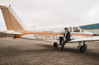 Senior portrait at a small hangar near Mobile International Airport in Mobile, Alabama — sitting
on the wing in a suit with brown dress shoes and aviator sunglasses.