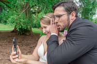 Bride and groom using a cell phone during their Los Angeles garden wedding, captured in a candid documentary moment with true to life color.