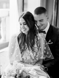 bride and groom sitting close together laughing with eyes closed in a soft black and white romantic portrait
